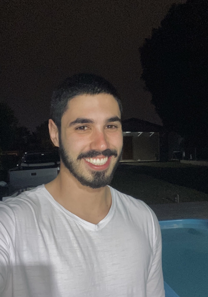 Homem jovem sorridente usando camiseta preta, posando com fundo amarelado.